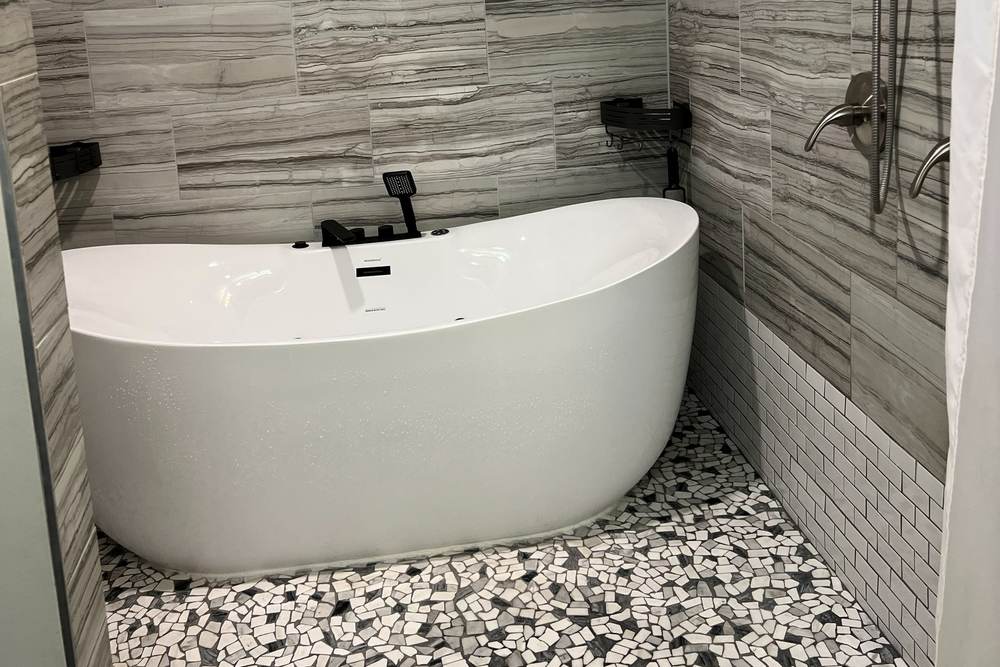 Freestanding tub on a black and white pebble floor in a tiled wet room we built in south Tulsa