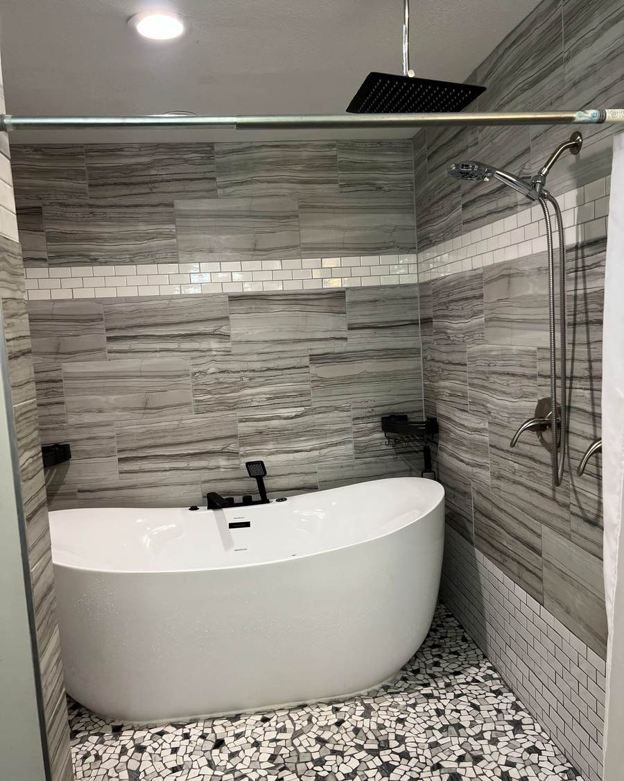Freestanding tub with a black tub filler in the tiled wet room of a south Tulsa bathroom