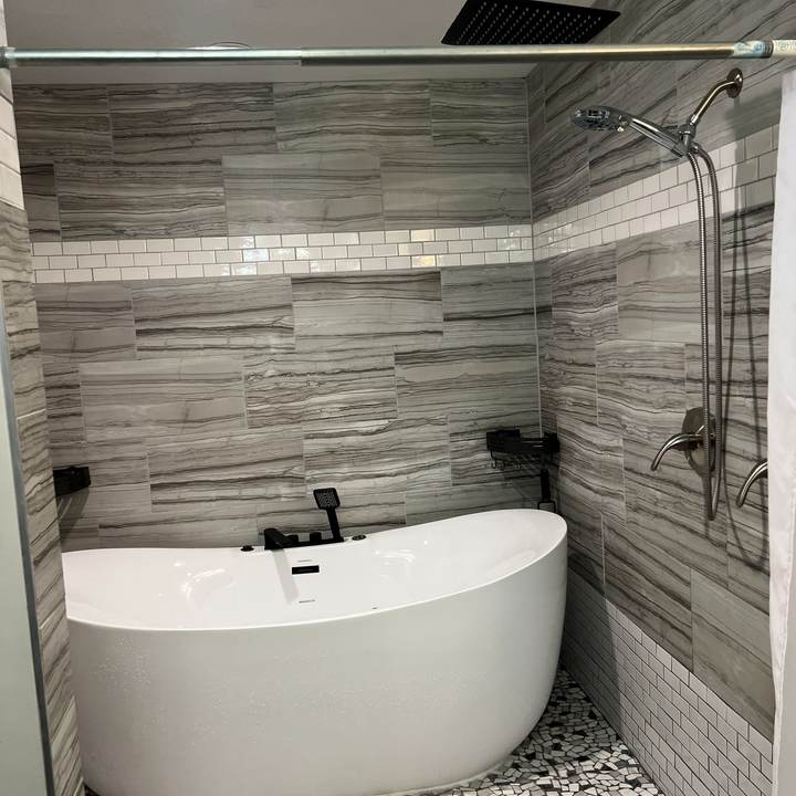 A freestanding tub with a black floor-mount filler in a tiled wet room
