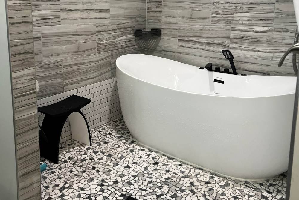 White freestanding soaking tub on a pebble floor with black fixtures, in a wet room we built in south Tulsa