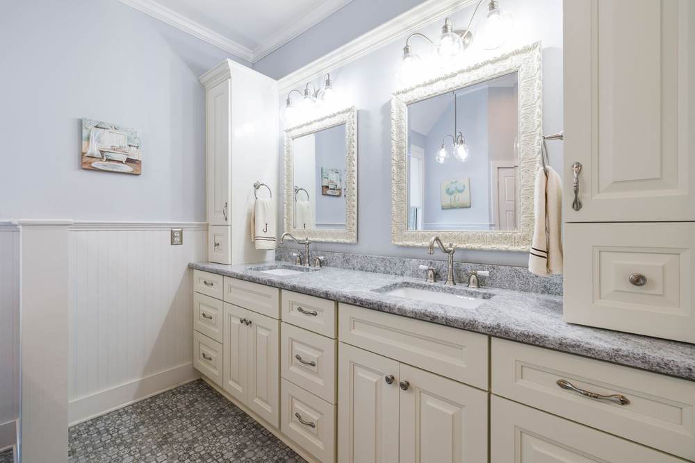 Long white double vanity with a granite top, two undermount sinks, framed mirrors and tall linen cabinets