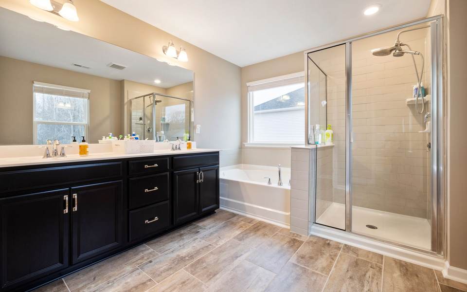 Primary bathroom with a dark double vanity, a drop-in soaking tub under a window and a framed glass shower stall