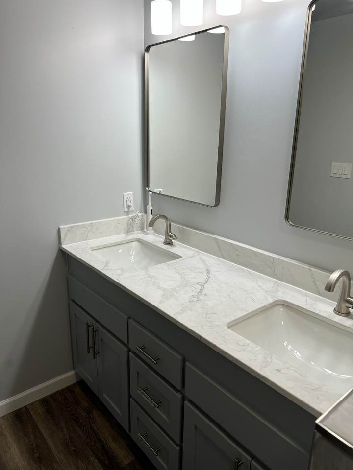 A gray vanity with a marble-look top, undermount sinks and a framed mirror