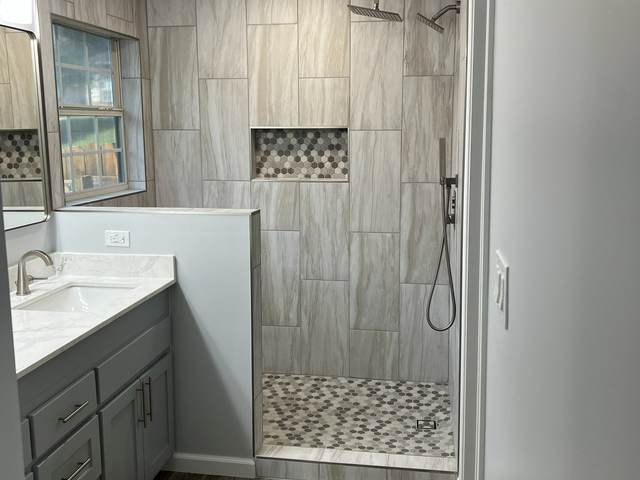 Walk-in shower behind a half wall beside a gray vanity, in a bathroom where a garden tub used to be