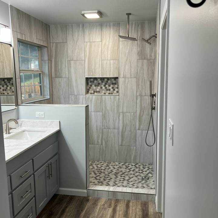 A walk-in shower behind a half wall next to a gray vanity and wood-look floor