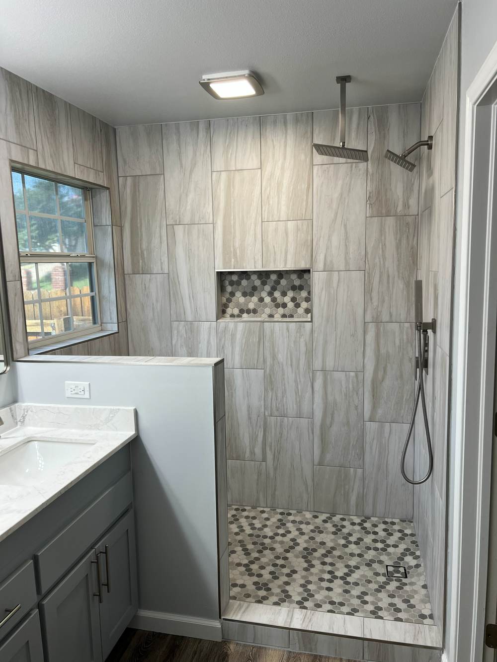 Finished walk-in shower with wood-look gray tile, a rain head and a hex-tile niche, built by our Tulsa team