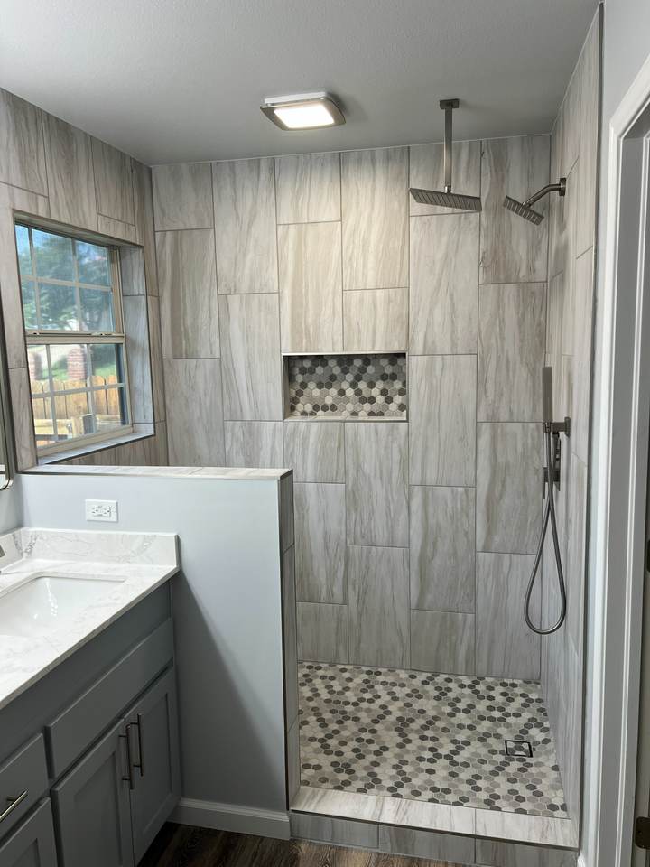 A walk-in shower with wood-look gray tile, a rain head and a hex-tile niche beside a window