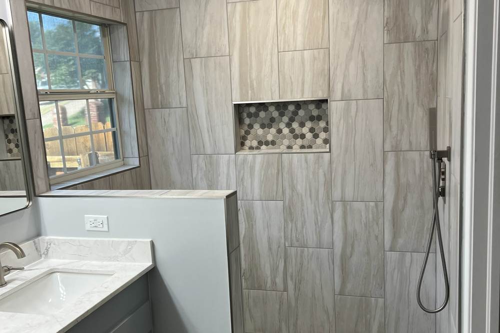 Tiled walk-in shower with a hex-tile niche, a half wall and a rain head, in an east Tulsa master bathroom we remodeled