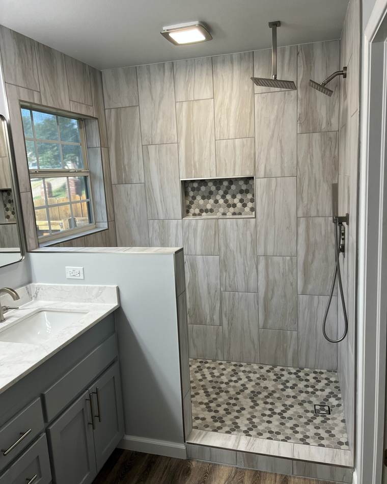 After: a tiled walk-in shower with a rain head, a hex-tile niche and a half wall beside a gray vanity