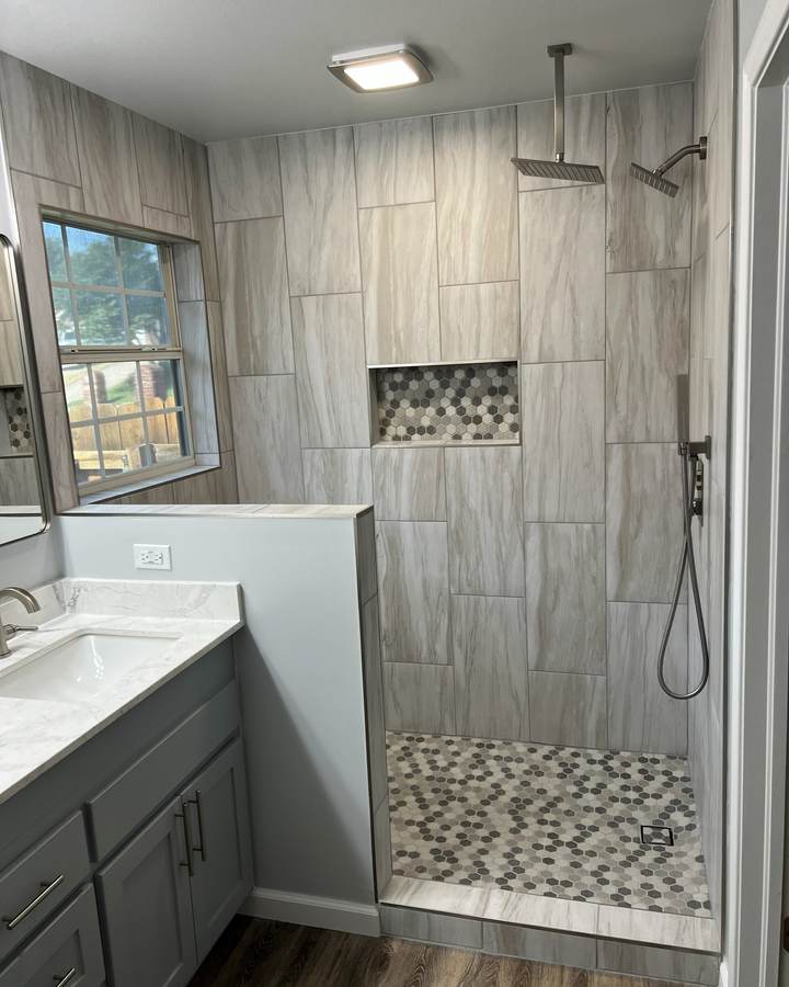 A walk-in shower with a rain head and a hex-tile niche beside a gray vanity
