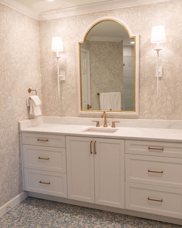 Primary bathroom with a white shaker vanity, a marble top, an arched gold mirror between two sconces and a blue mosaic tile floor