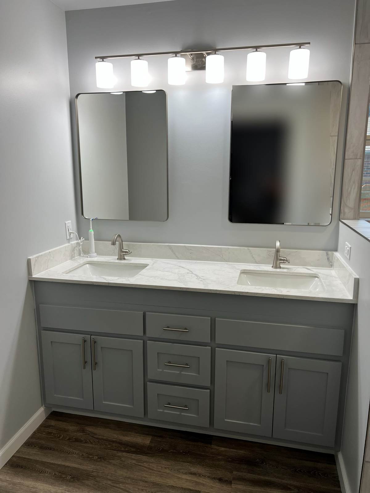 After: the vanity refinished in gray with new doors, a quartz top, two mirrors and a new light bar