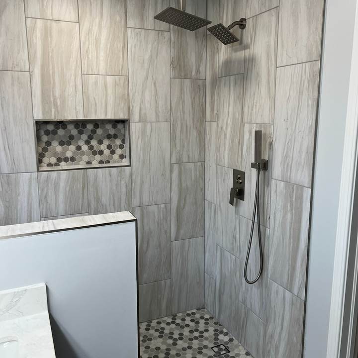 A rain shower head and handheld shower with matte black trim on wood-look gray tile