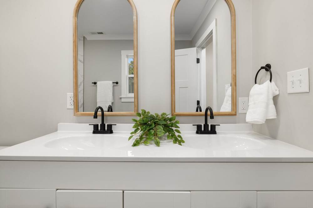 White double vanity with a one-piece molded top, two built-in bowls and matte black faucets under arched wood mirrors