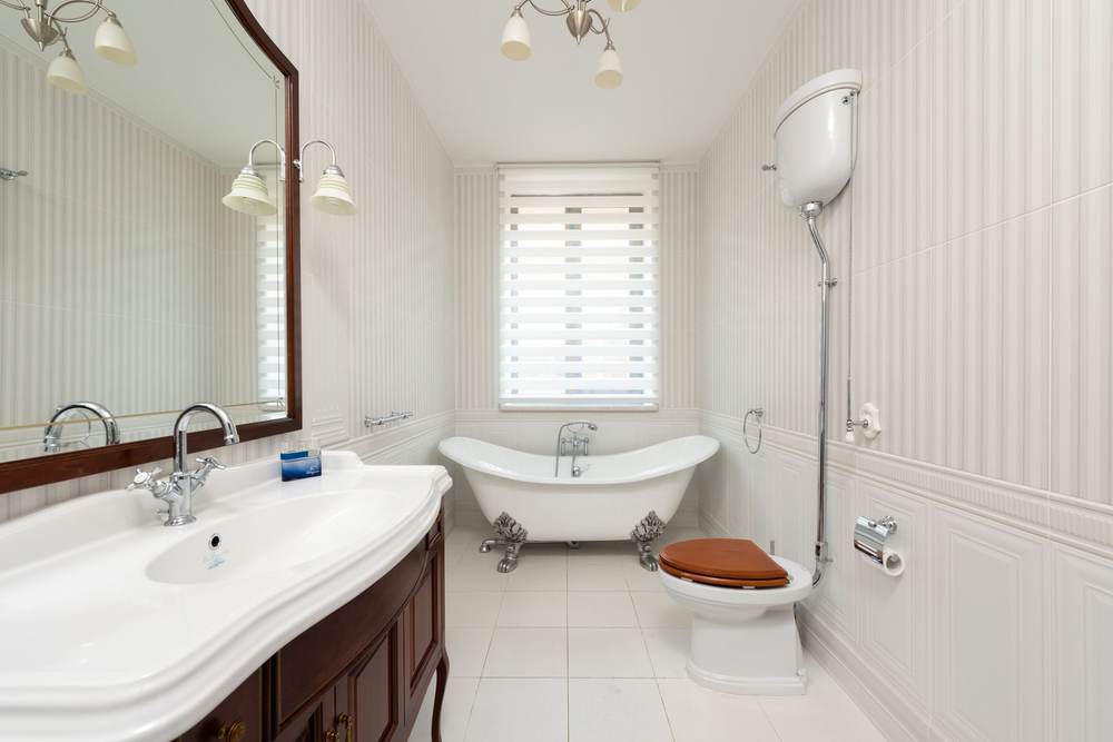 Bathroom in a classic style with a clawfoot tub under a window, a high-tank toilet and white paneled wall tile