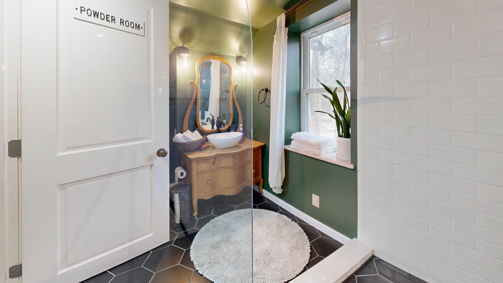 Powder room with an antique dresser made into a vanity, a vessel sink, a gold-framed mirror and a dark hex tile floor