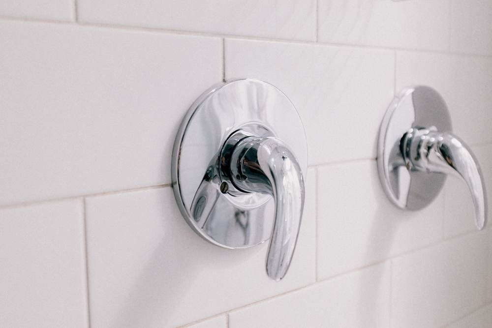 Chrome single-lever shower valve trim on white subway tile, beside a second lever control