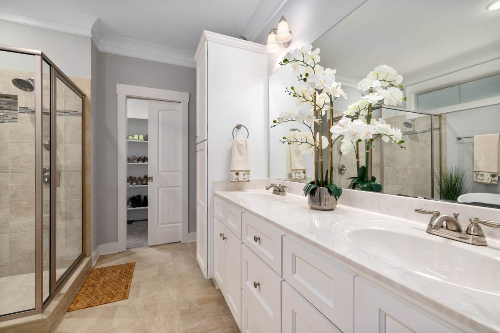 Primary bathroom of the kind many 2000s houses have now: a framed glass shower stall, a white double vanity with a cultured-marble top and a beige tile floor
