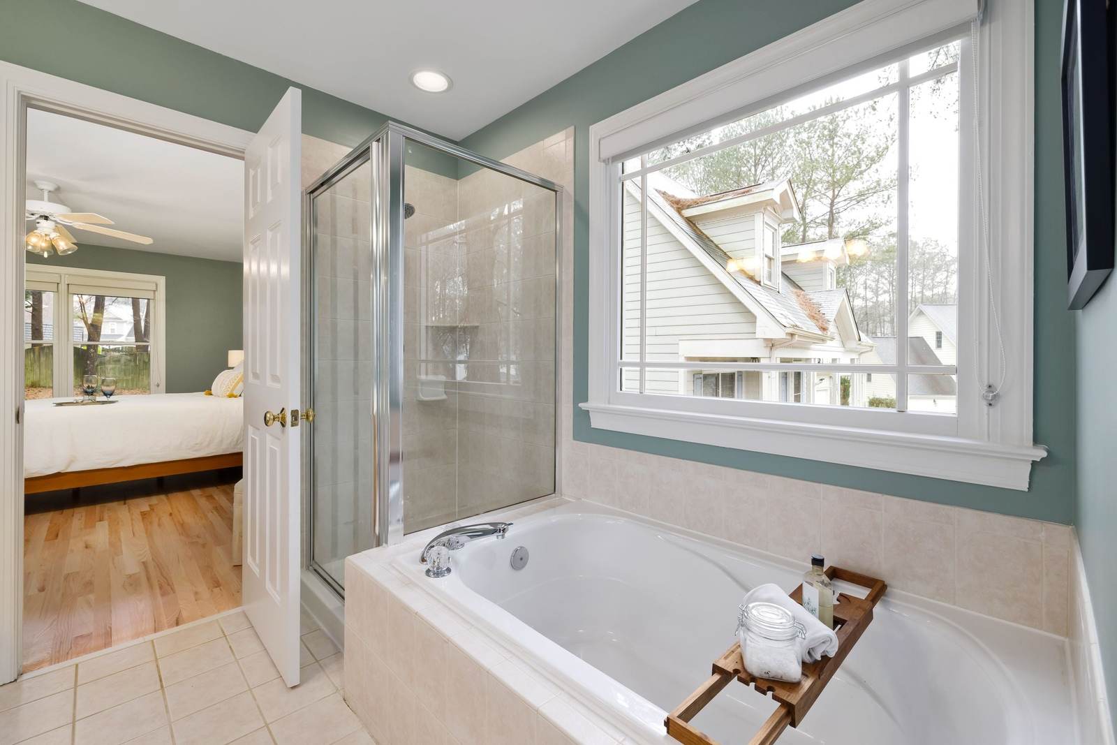 A primary bathroom like many from the 1990s and 2000s: a framed glass shower stall beside a drop-in jetted tub under a window