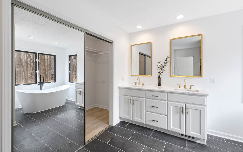 Bright primary bathroom with a white double vanity, gold mirrors and a freestanding tub by the windows