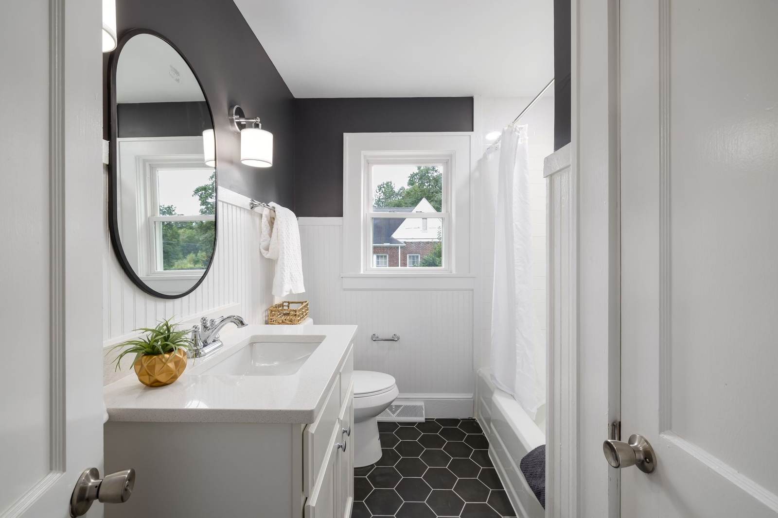 Small white bathroom with beadboard wainscot, a black hex tile floor, a toilet beside the vanity and a tub behind a curtain