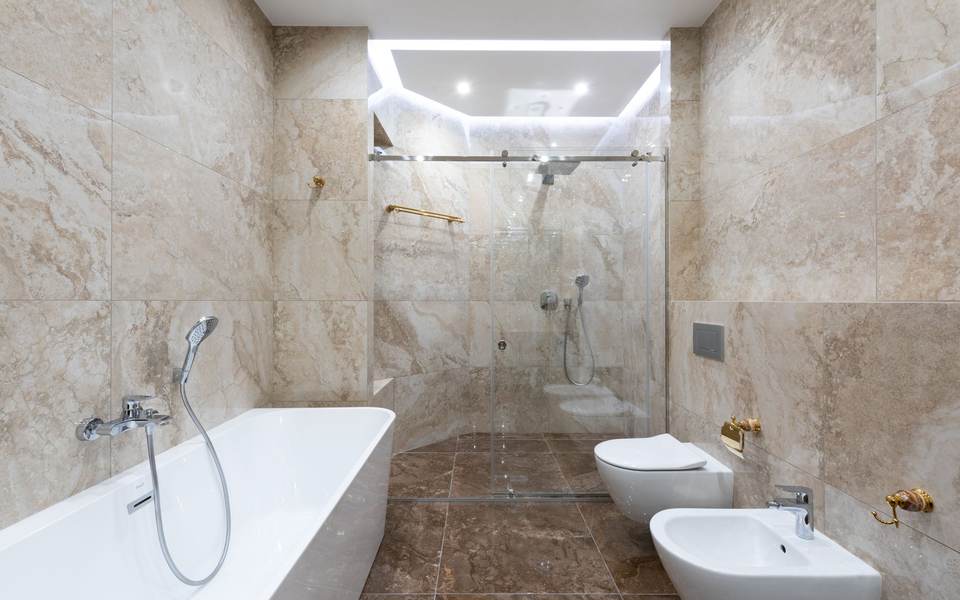 Marble-look bathroom with a white tub, a glass walk-in shower, a wall-hung toilet and a bidet