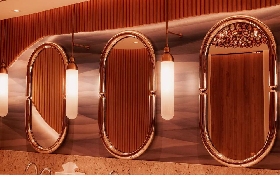 Restaurant restroom with copper-framed oval mirrors and pendant lights over a stone counter