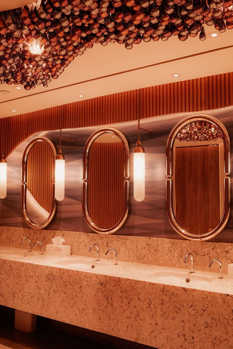 Restaurant restroom with copper-framed oval mirrors and pendant lights over a stone counter