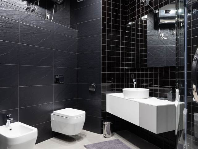 Wall-hung toilet against black tile walls in a modern restroom