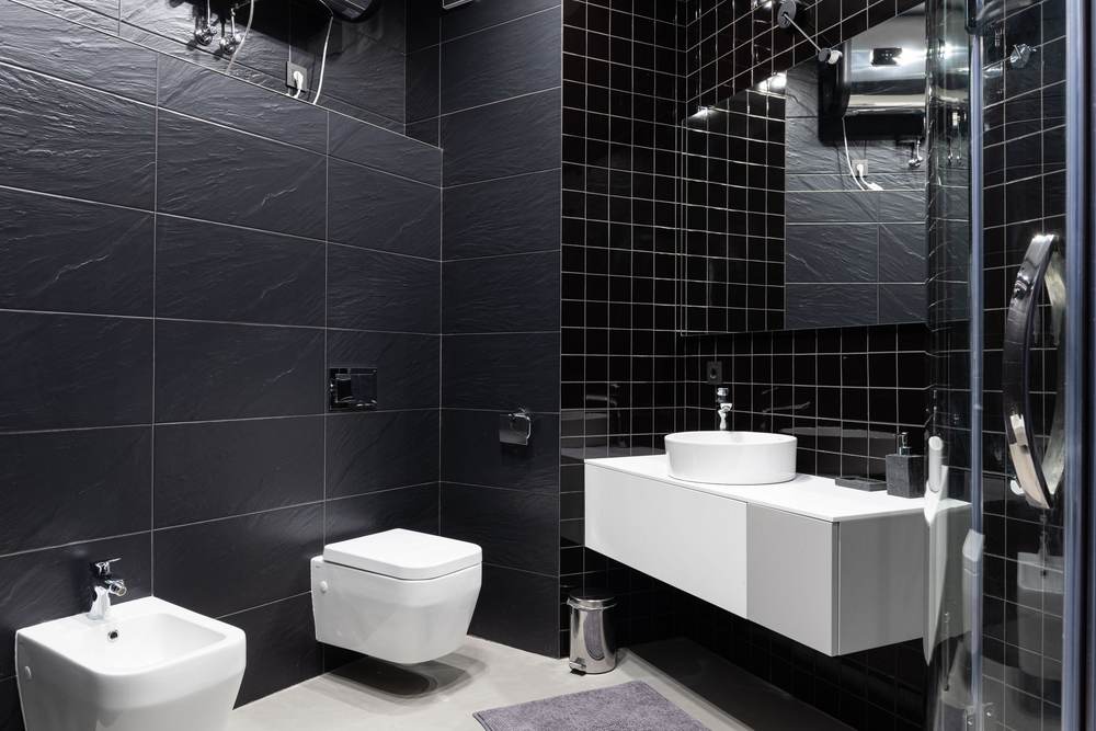 Restroom with black tile walls, a wall-hung toilet and a floating white vanity