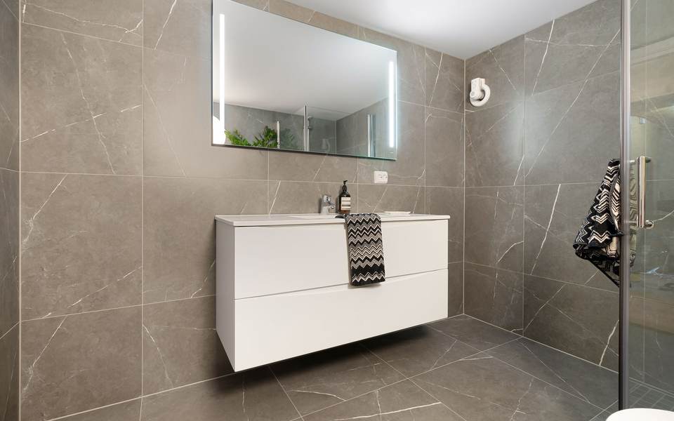 Restroom with large gray porcelain wall tile, a floating white vanity and a lit mirror