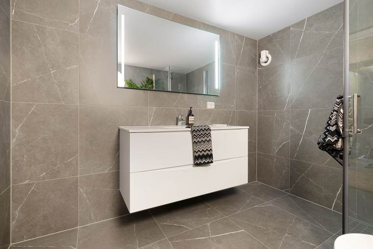 Restroom with large gray wall tile, a floating white vanity and a lit mirror