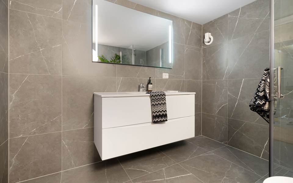 Bathroom with large gray porcelain wall tile, a white floating vanity and a lit mirror