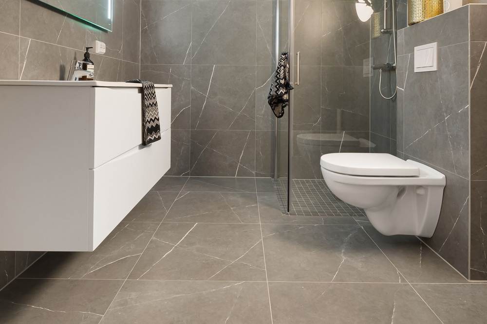 Gray porcelain tiles in large slabs across the floor and walls of a bathroom with a wall-hung toilet and floating vanity