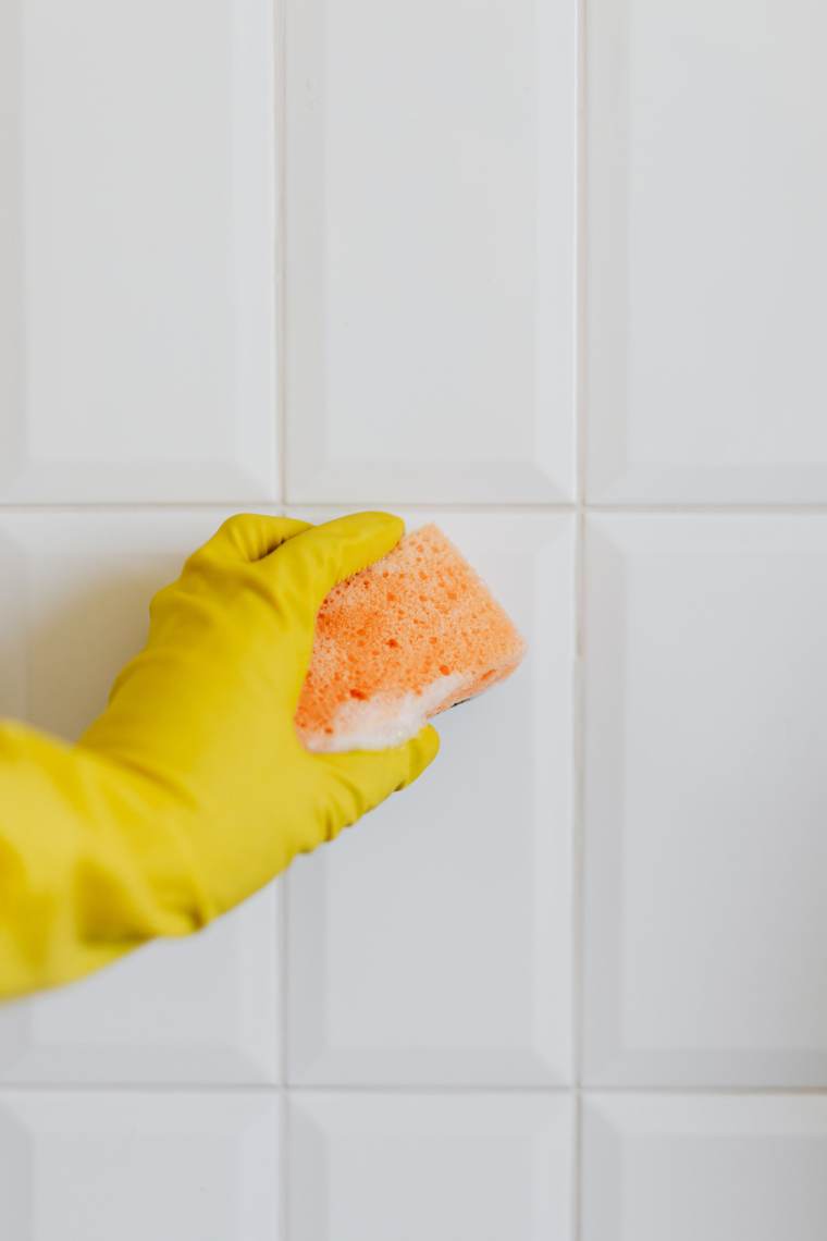 Gloved hand wiping white wall tile with a sponge