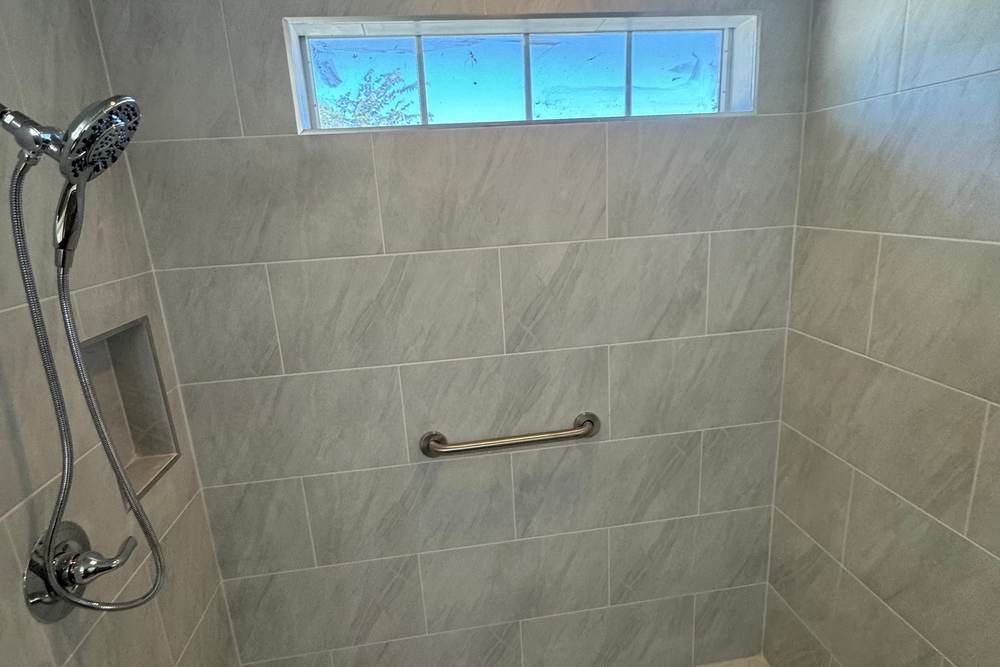 Roll-in shower with a hand shower, a niche, a grab bar and a white hex floor, built for a U.S. military veteran in Glenpool
