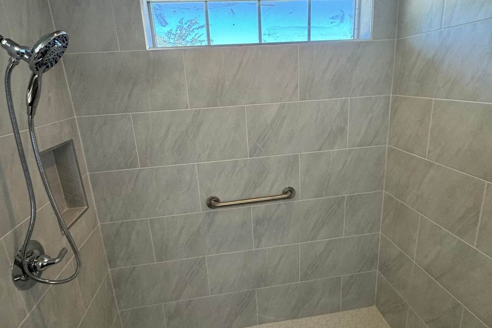 Roll-in shower with large gray tile, a white hex floor and a niche, built where a corner jetted tub used to be, for a U.S. military veteran in Glenpool