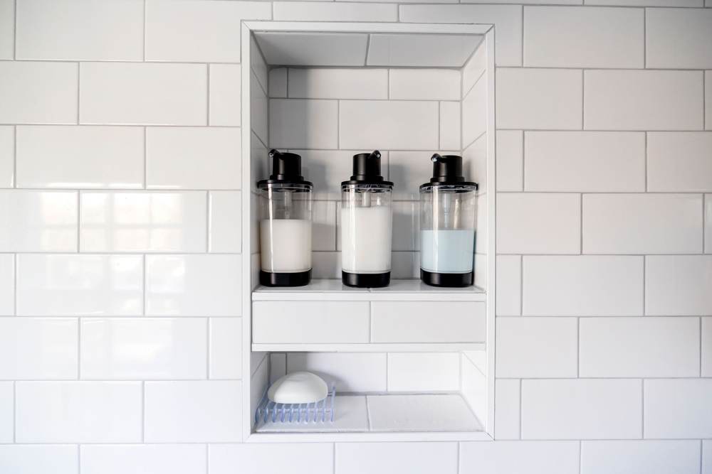 Recessed shower niche framed in whole white subway tiles, with a tiled shelf across it and bottles on both levels