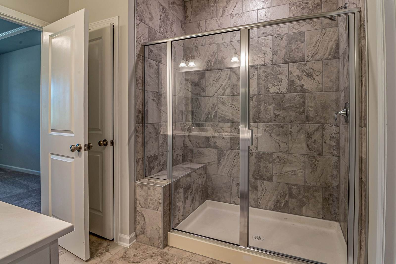 Builder-grade shower with gray tile walls, a framed glass door and a white acrylic base, the kind many newer homes came with