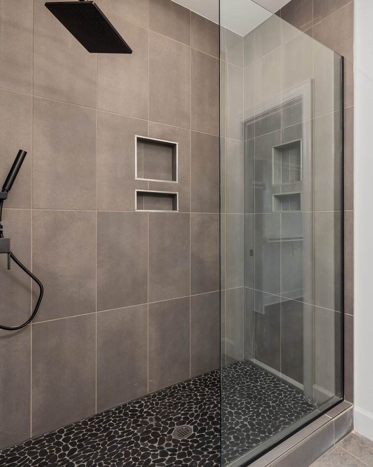 Walk-in shower with large gray wall tile, a black pebble floor, a frameless glass panel and matte black fixtures