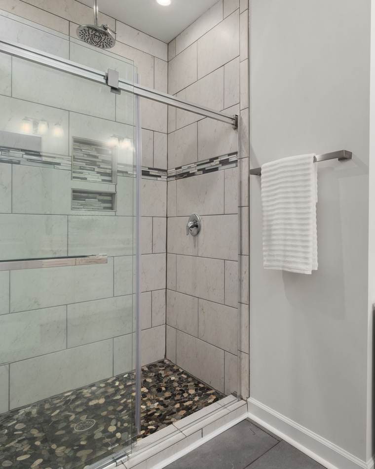 Tiled walk-in shower with a single-handle valve, a rain head, a pebble floor and a sliding glass door