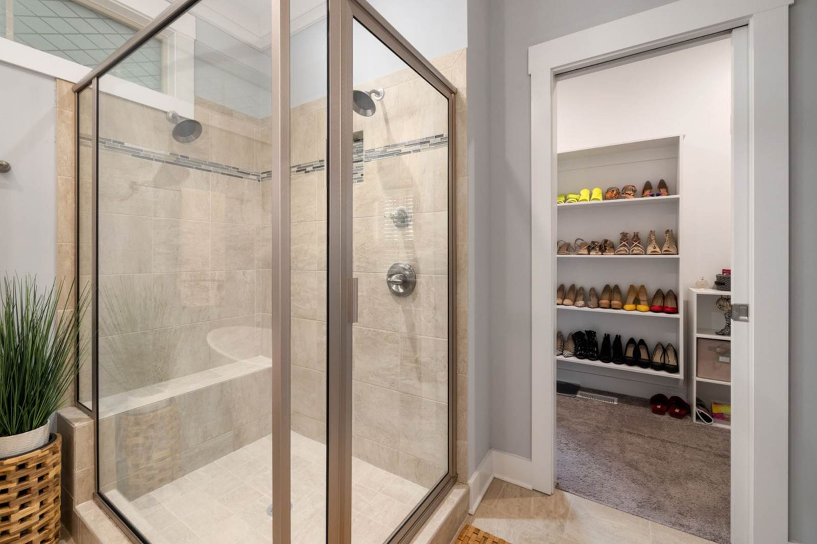 Tiled shower with a corner bench, two shower heads and a framed glass enclosure beside the door to a walk-in closet