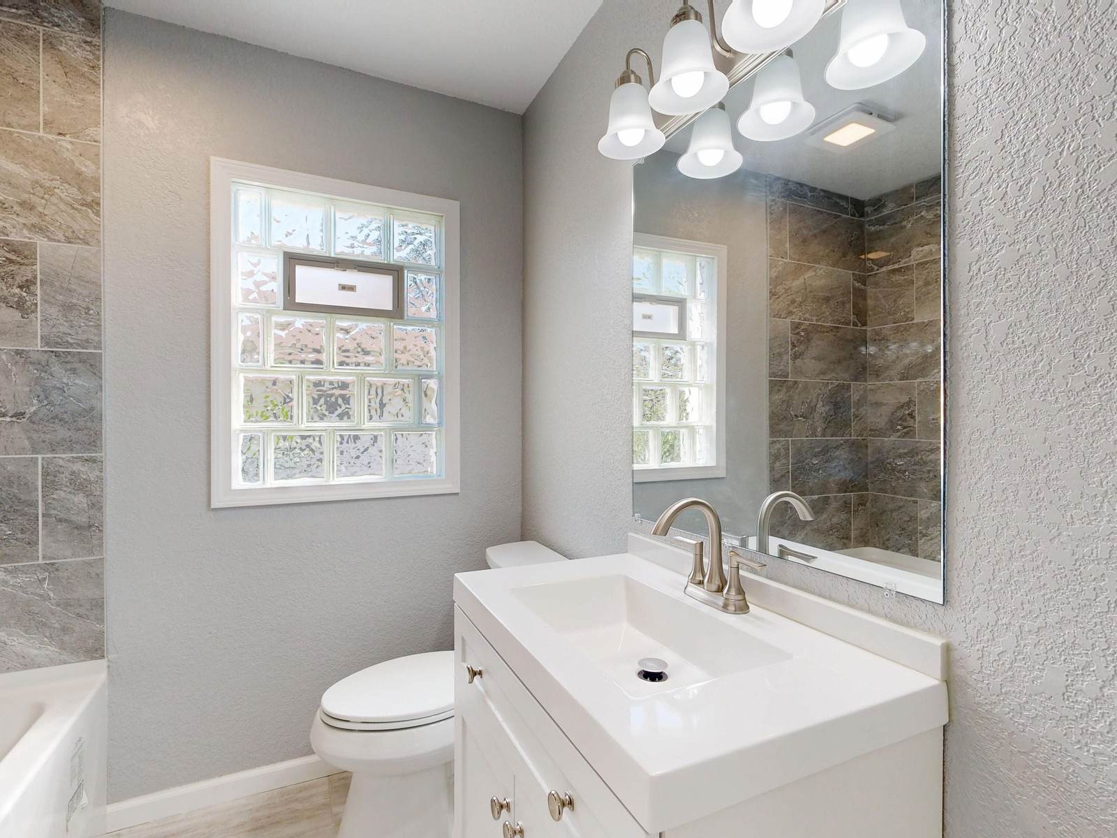 Small hall bathroom with a glass block window, a white vanity and a tiled tub and shower