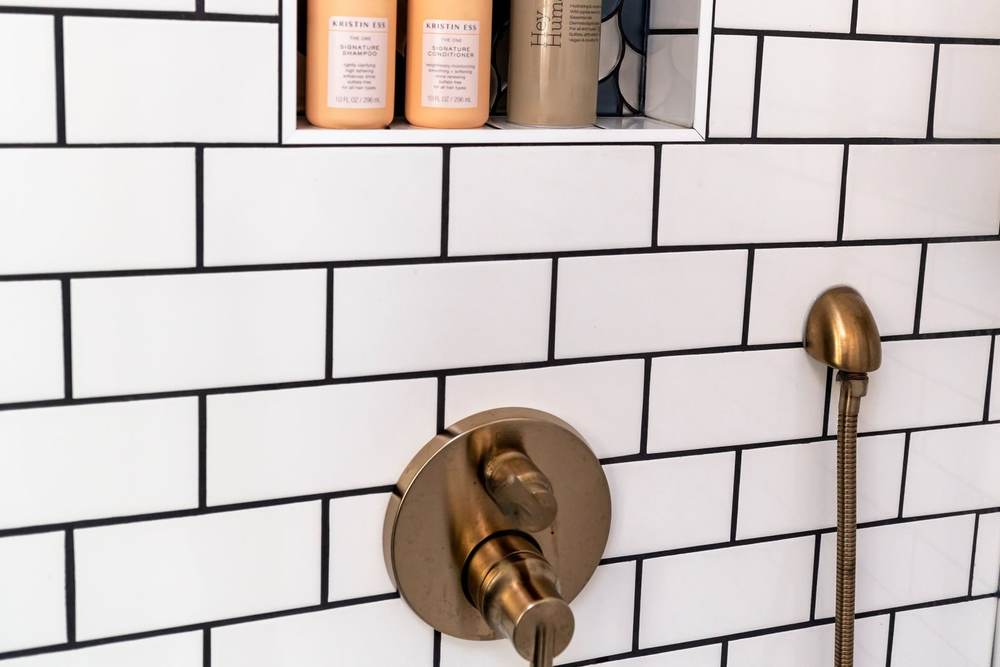 Brushed brass shower valve trim with a lever and a diverter, a hand shower hose and a tiled niche above it