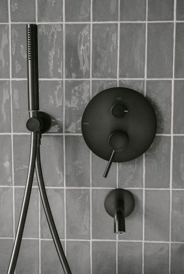 Matte black shower valve trim and hand shower hose on gray wall tile