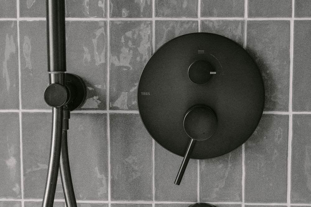 Matte black shower valve trim and a hand shower on a slim holder against gray glazed tile
