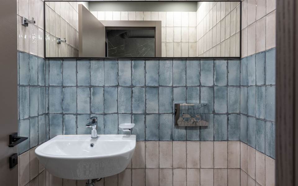 Single-user restroom with blue tile walls, a wall-mounted sink and a long mirror
