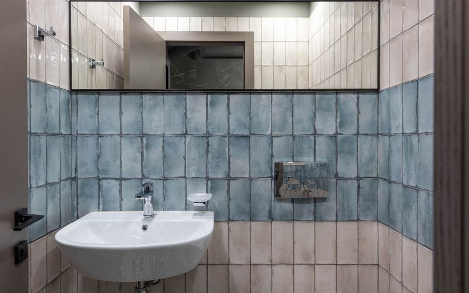 Single-user restroom with blue tile walls, a wall-hung sink and a long mirror