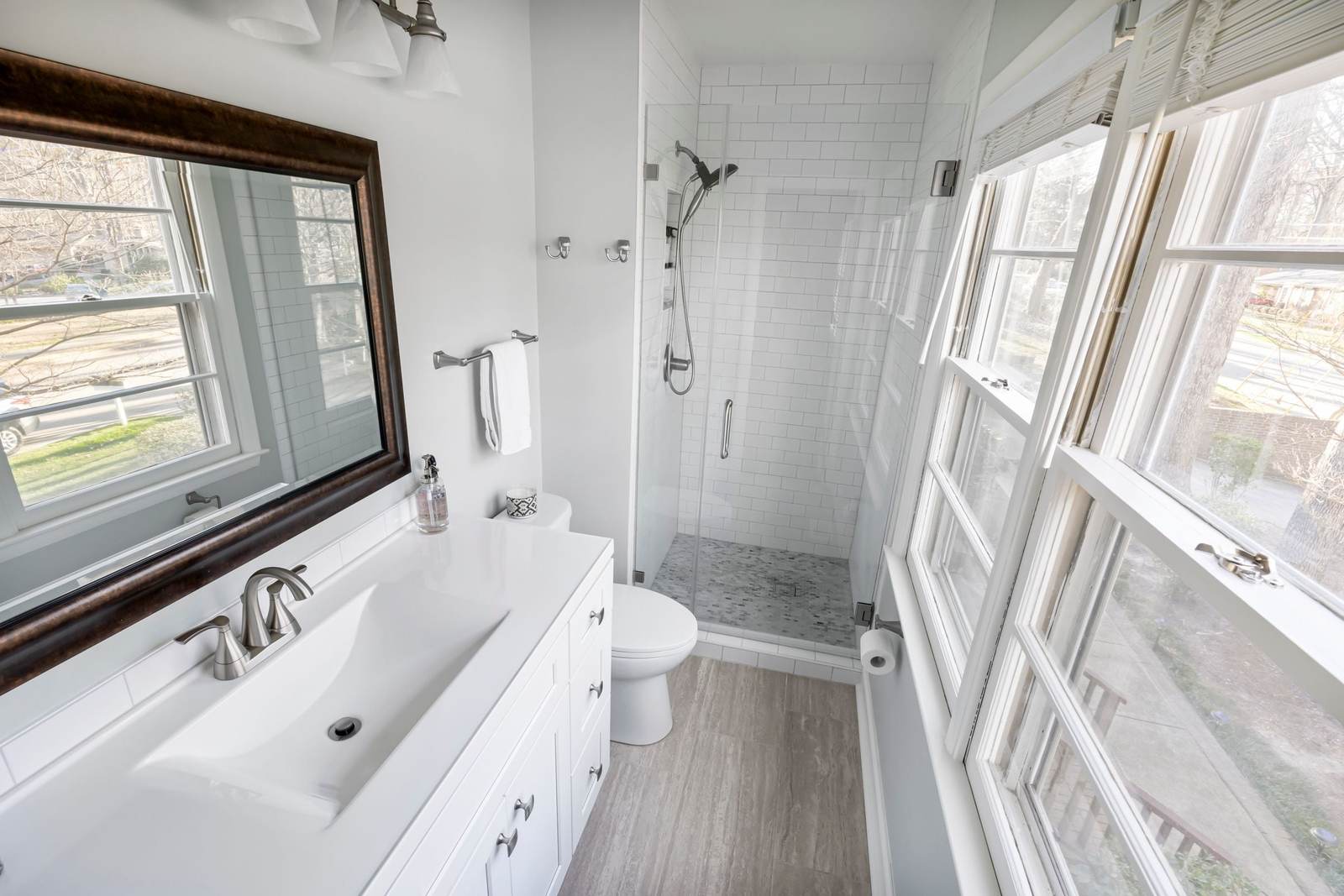 Small bathroom with a white subway tile walk-in shower behind a glass door, a white vanity and a row of tall windows