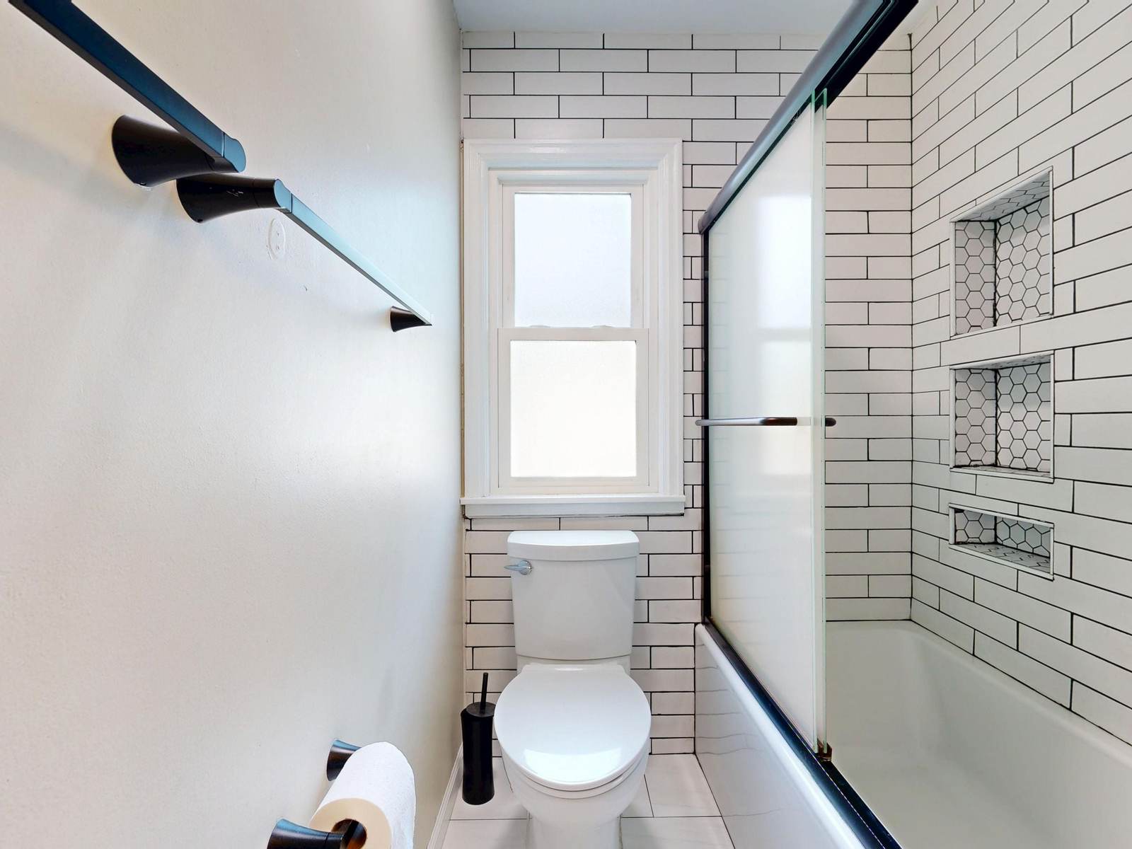 Small bathroom with white subway tile, a tub with a sliding glass door, three tiled niches and a window over the toilet
